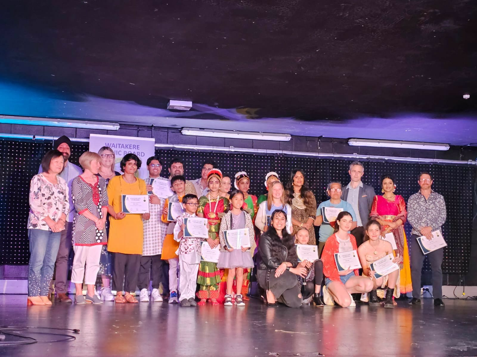 Large group of performers and guests on stage holding certificates