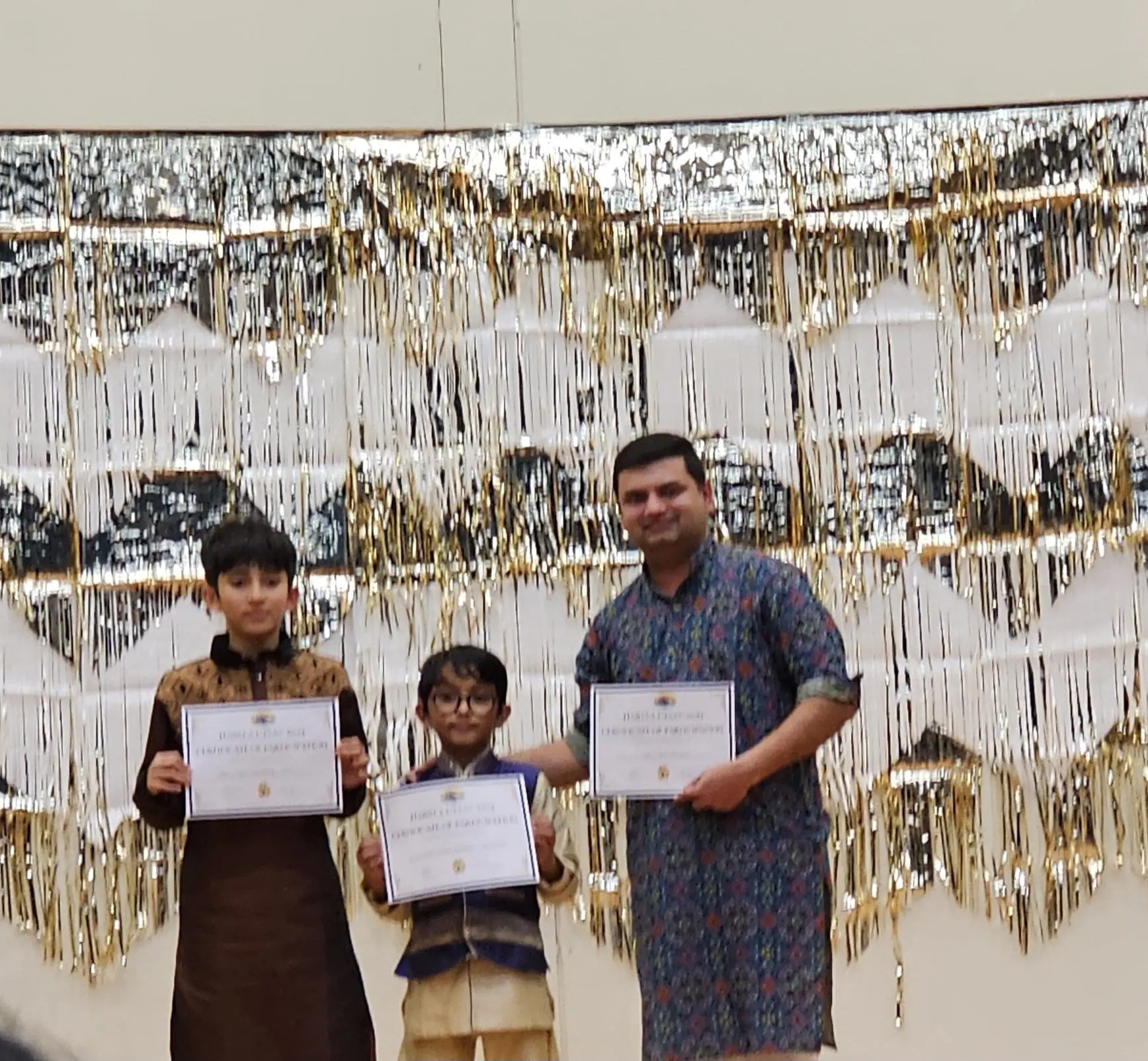Two students and their teacher holding festival certificates on stage